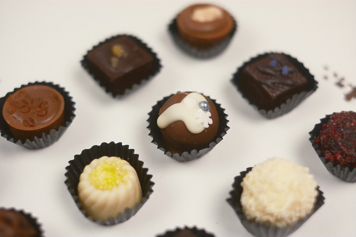 An assortment of gourmet chocolate truffles and pralines in black paper cups, arranged on a clean white surface with a shallow depth of field.