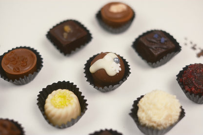 An assortment of gourmet chocolate truffles and pralines in black paper cups, arranged on a clean white surface with a shallow depth of field.
