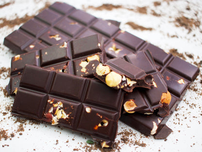 image shows a close up of broken up hand made sugar free dark chocolate bar embedded with hazelnuts.