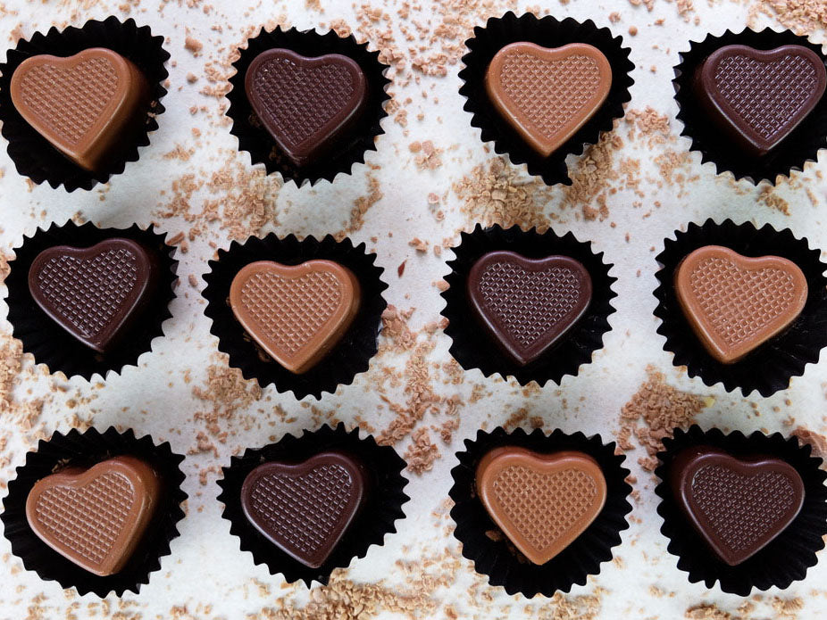 Image shows a collection of 6 milk chocolate and 6 dark chocolate, hand made chocolate hearts that are filled with caramel.