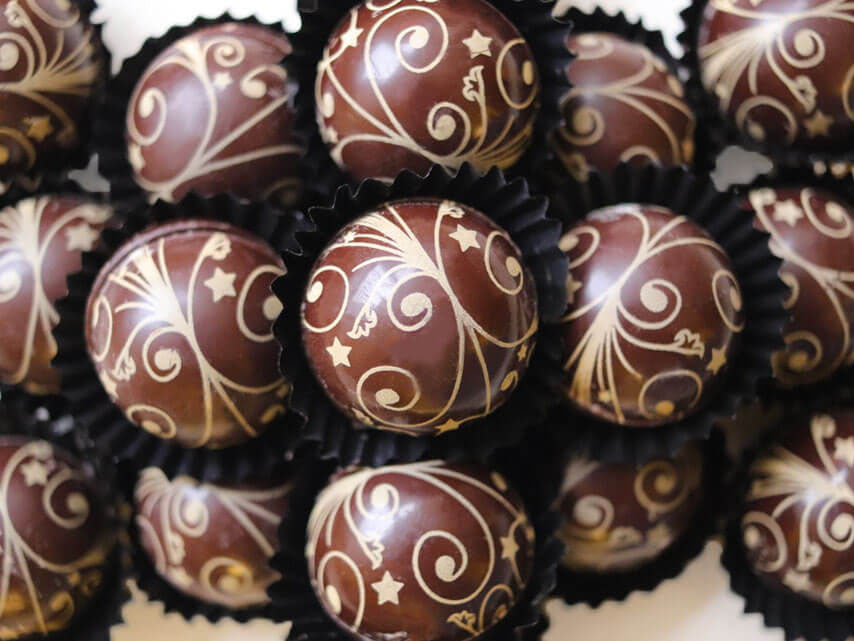 Image shows a collection of hand made Cherry and Kirsch Liqueur truffles decorated with edible gold swirls and stars
