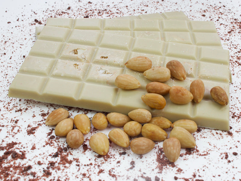 image shows a close up of 100g hand made vegan white chocolate bars embedded with almonds, and with extra almonds scattered on top