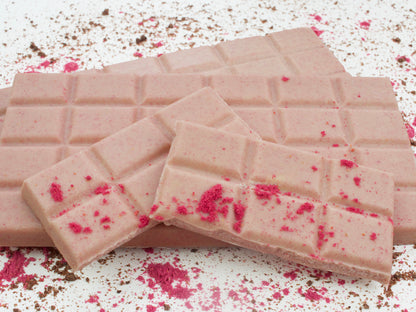 image shows close up of 100g hand made vegan white raspberry bars with broken pieces and a raspberry sprinkle